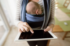parent carrying baby and looking at tablet